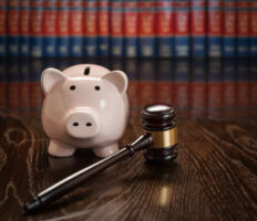 Gavel and Piggy Bank on Wooden Table With Law Books In Background.